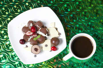 Chocolate fudge garnished with chocolate, mint and cranberries. Lies on a white plate, on a green background.