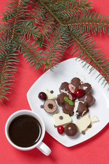 Chocolate fudge garnished with chocolate, mint and cranberries. Lies on a white plate, on a white background. Nearby a cup of coffee and a branch of spruce.