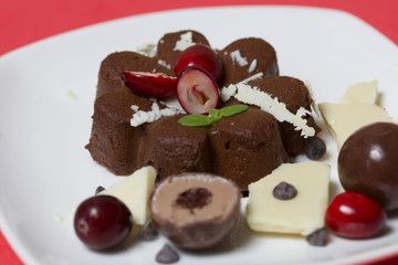 Chocolate fudge garnished with chocolate, mint and cranberries. Lies on a white plate, on a coral background.