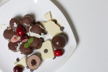 Chocolate fudge garnished with chocolate, mint and cranberries. Lies on a white plate, on a white background.