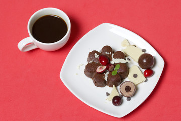 Chocolate fudge garnished with chocolate, mint and cranberries. Lies on a white plate, on a coral background. Near a cup of coffee.