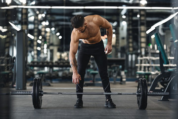 Strong bodybuilder going to exercise with barbells at gym