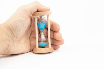 Hand holding hourglass isolated on white. Blue sand, wooden clock.