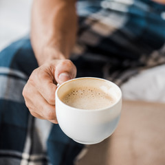 cropped view of bi-racial man holding cup of coffee in morning