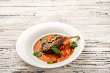 Vegetable soup with tomatoes in a restaurant close-up. Lamb soup on bone noodles on a white plate and copy space.
