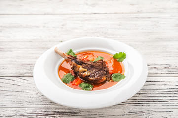 Vegetable soup with tomatoes in a restaurant close-up. Lamb soup on bone noodles on a white plate and copy space.