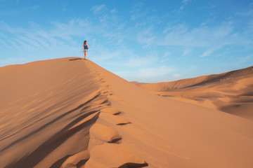 Fototapeta na wymiar Young girl walking through the dunes in sahara desert in Morocco