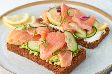 Smorrebrod - traditional Danish sandwiches. Black rye bread with salmon, cream cheese, cucumber, avocado on wooden background, close up
