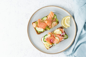 Smorrebrod - traditional Danish sandwiches. Black rye bread with salmon, cream cheese, cucumber, avocado on wooden background, top view, copy space