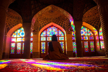 Naklejka na ściany i meble Shiraz, Iran. Girl sits on the floor and looks at the sunlit stained-glass windows in the morning sun in the Nasir-ol-molk Mosque.