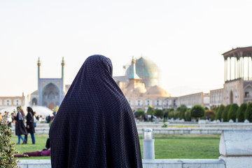 Woman in black chador looks at the Shah Mosque (also known as the New Abbasi Mosque or Royal Mosque) on the Naghsh-e Jahan Square. Back view.