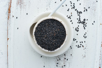 Black Sesame on white bowl with spoon. White wooden background. Top view, close up. Copy space.
