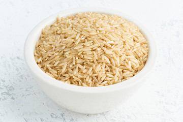 Brown rice in white bowl on white background. Dried cereals in cup, vegan food, fodmap diet. Side view, close up.