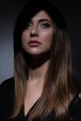 Young beautiful woman in black dress with a serious facial expression shot in the studio in the shadows. Studio shot.