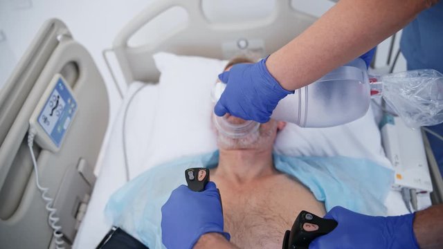 Doctor resuscitating patient in hospital. Close up of doctor defibrillating senior patient in hospital