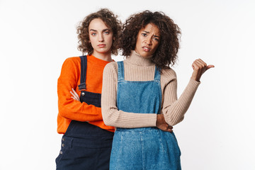 Portrait of displeased multinational women pointing thumb aside