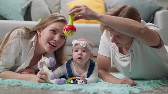 Little girl kid plays a rattle on the floor with parents