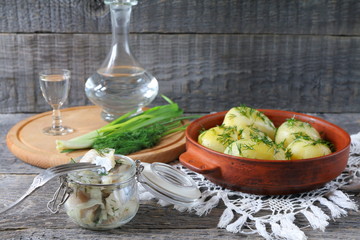 On the table is jar of salted herring near the plate with boiled potatoes and fresh greens.