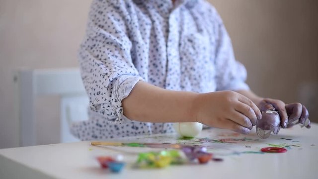 A litle child peels the shell of a painted Easter egg.