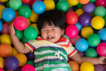 Fototapeta na wymiar Happy Asian girl (one and half years olds) big smile and playing little colorful balls in pool ball. The concept of playing is the best learning for children.