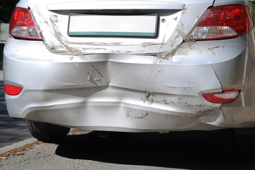 Close-up wrecked rear bumper and tail lights of new modern grey car after vehicle accident on road at bright sunny day
