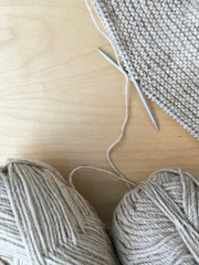 Knitting. Top view on balls of natural wool for hand knitting and handmade beige fabric on wooden...