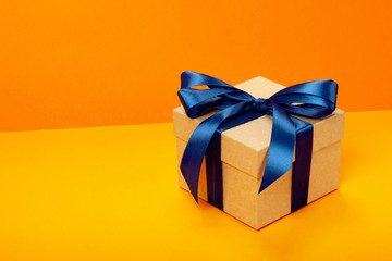 Trendy attractive minimalistic gift with blue bow on the orange background. Merry Christmas, St. Valentine's Day, Happy Birthday and other holidays concept. Copy space.