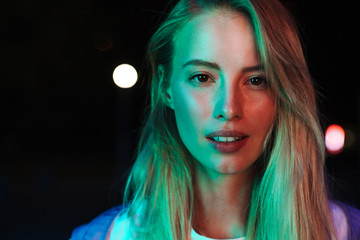 Image of woman looking at camera over bright neon lightening at night