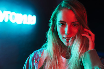 Image of young woman standing over multicolored neon text sign outdoors