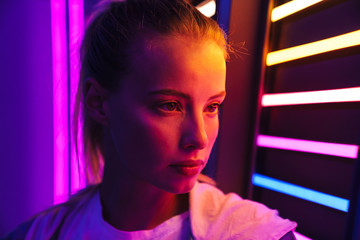 Image of young woman standing by multicolored neon illumination indoors