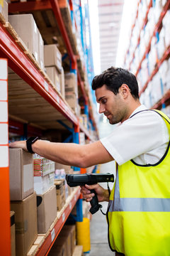 Warehouse manager with yellow coat scanning barcode on box 