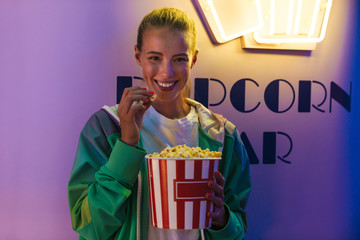 Image of caucasian woman smiling and eating popcorn in cinema indoors