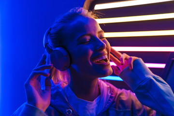 Image of woman listening to music with headphones over neon illumination