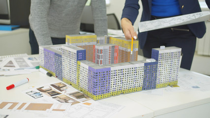 Engineer with scheme in hand shows models of houses and explain something to workmate