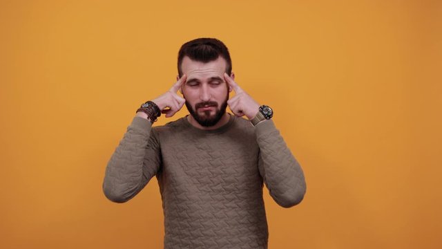 Handsome caucasian man over isolated orange background keeping fingers on head, thinking about issue, headache wearing casual green sweater