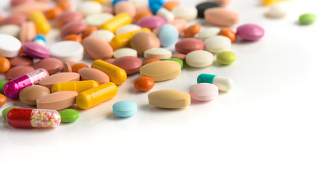 A lot of Different colorful pills on a white table background. Medicinal tablets, capsules, pills.