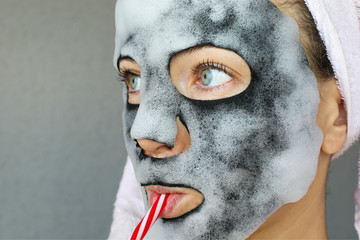 Bubble charcoal oxygen face mask. Beautiful young woman with bubbling carbonated mask and towel on the head. Face treatment.