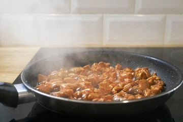 Chicken fillet fried in black pan at the home kitchen with selective focus. Smoke cooking