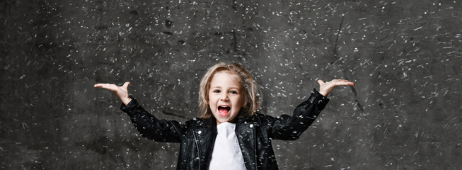 Fototapeta na wymiar Happy screaming kid girl is posing with her hands up spread with open palms under the snow with free copy space. Banner