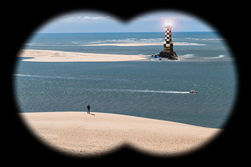 Man Standing on the Beach with a Lighthouse seen through Binoculars