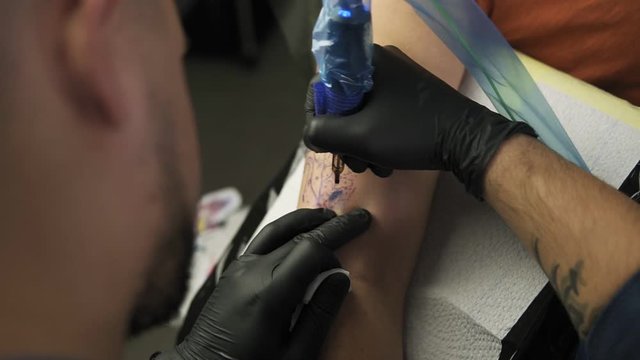 A close-up of a tattoo artist makes a tattoo on a woman's arm. A high resolution. Professional tattooist works in studio. High angle footage from the shoulder of master