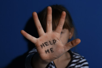 Abused little girl showing with phrase HELP ME near blue wall, focus on hand. Domestic violence...