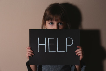 Abused little girl with sign HELP near beige wall. Domestic violence concept