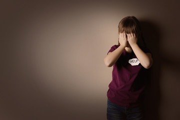 Little girl with sign HELP on beige background, space for text. Child in danger