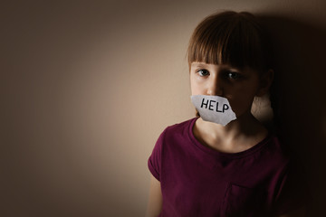 Sad little girl with sign HELP on beige background, space for text. Child in danger