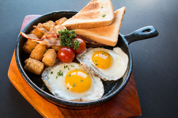 Scrambled egg skillet with toast,hash brown,tomatoes on a black background and wooden plate,