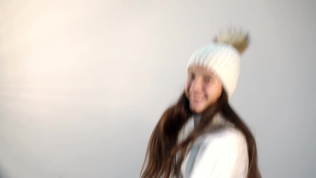 happy long haired teenage girl in loose white sweater and knitted hat dances jumping on light background closeup