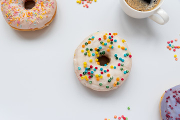 Cups of espresso coffee and sweet donuts decorated colorful sprinkles on white background. Flat lay. Top view. Unhealthy food