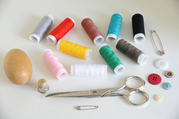 Accessories for tailoring on white table - Scissor , scissors, buttons, needle and thread, spools of colored threads