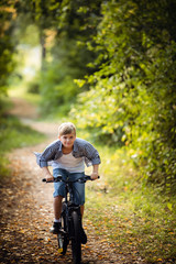 A young boy riding his bike in a summer forest.